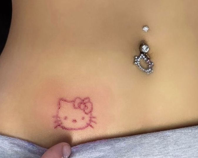 a hello kitty tattoo on the side of a woman's stomach with a diamond ring