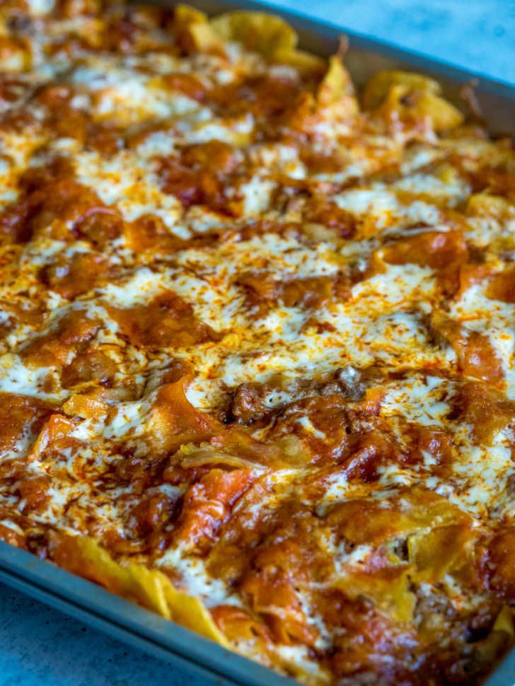 a casserole dish with cheese and sauce in it sitting on a blue table