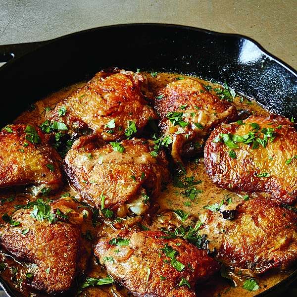 a skillet filled with meat covered in sauce and parsley on top of a table