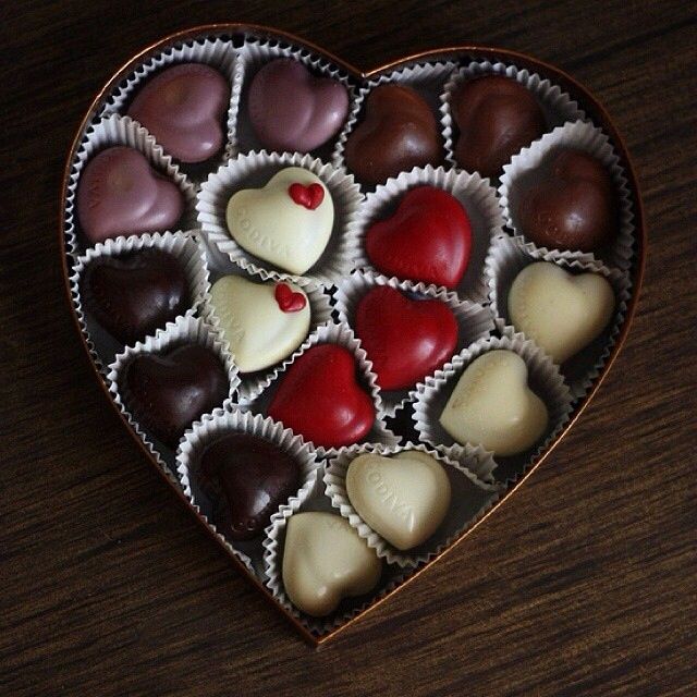 a heart shaped box filled with assorted chocolates on top of a wooden table