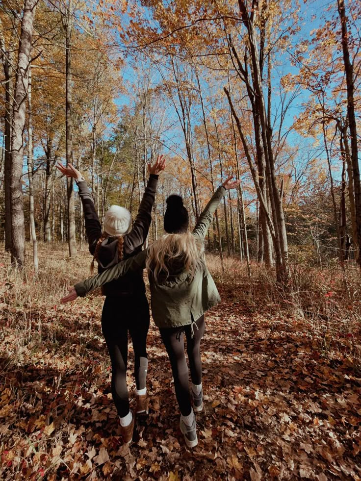 two people are walking through the woods with their arms in the air