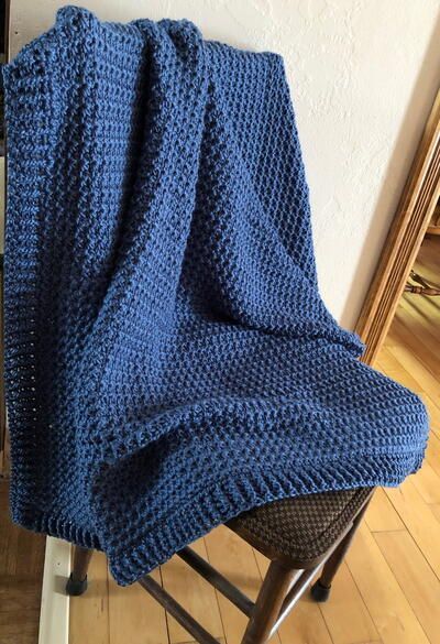 a blue knitted blanket sitting on top of a chair