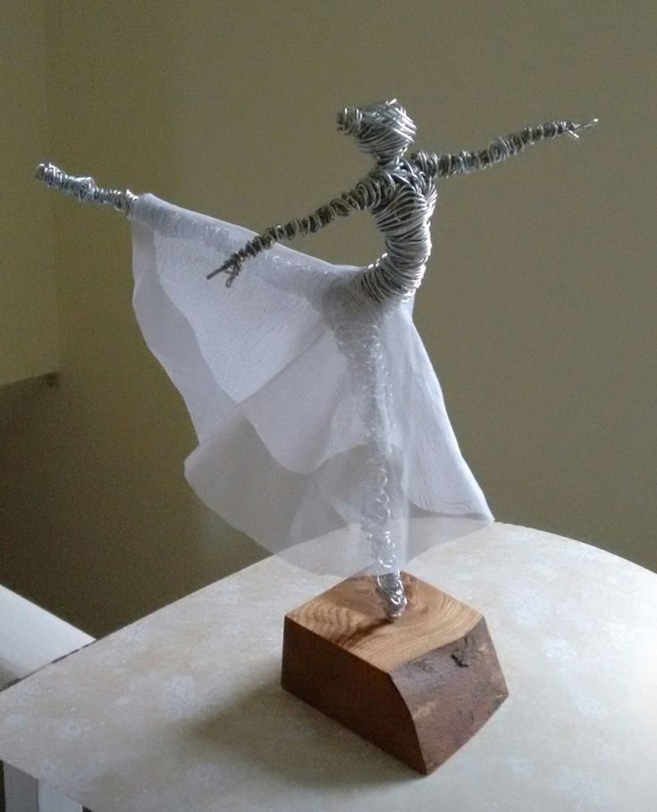 a sculpture of a woman in white dress on top of a wooden block with her arms stretched out