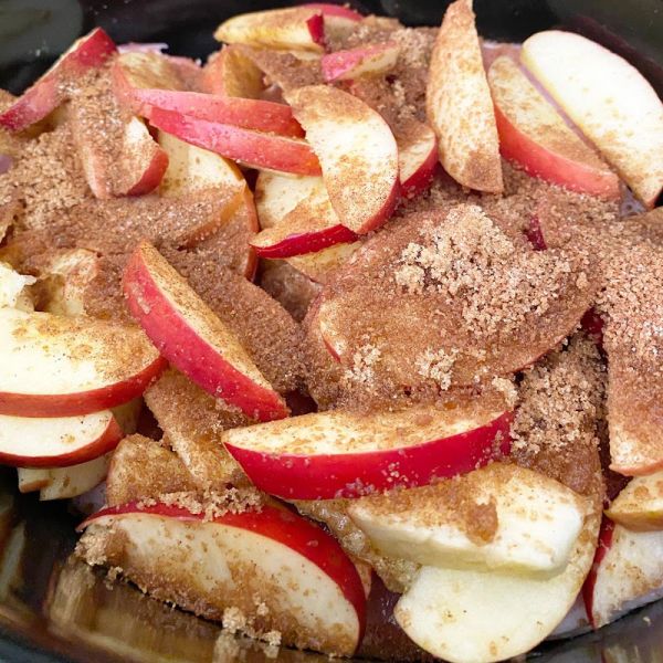 sliced apples and cinnamon in a crock pot with sugar on the top, ready to be cooked