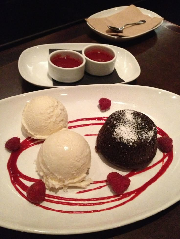 two desserts on a white plate with raspberries and ice cream in the middle