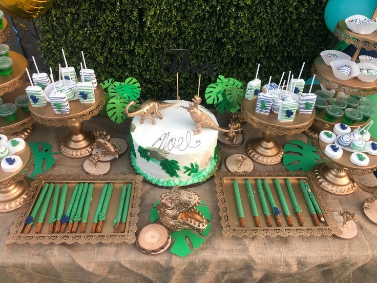 a table topped with lots of desserts and cake covered in green frosted icing