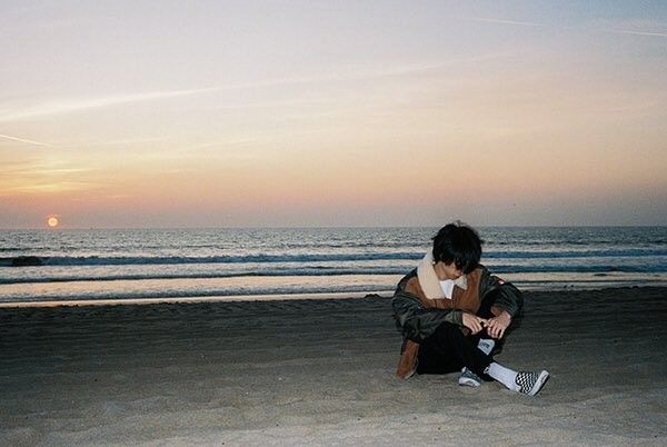 a man sitting on top of a sandy beach next to the ocean at sunset or dawn