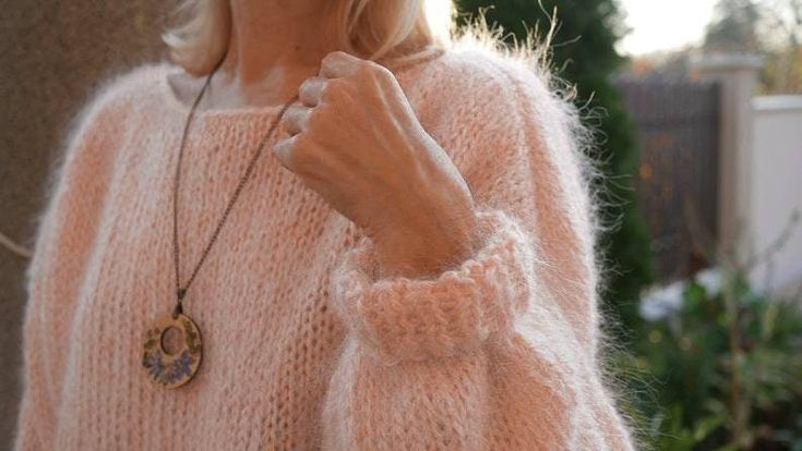 a woman in a pink sweater is holding her hand up to her ear