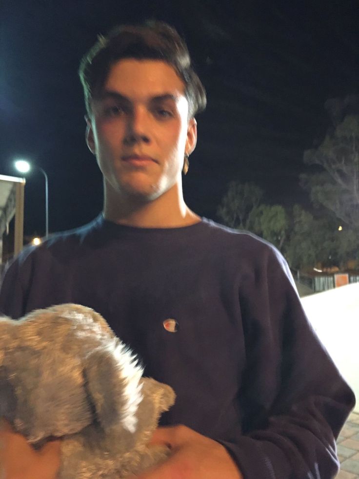 a young man holding a stuffed animal in his hands at night time with street lights behind him