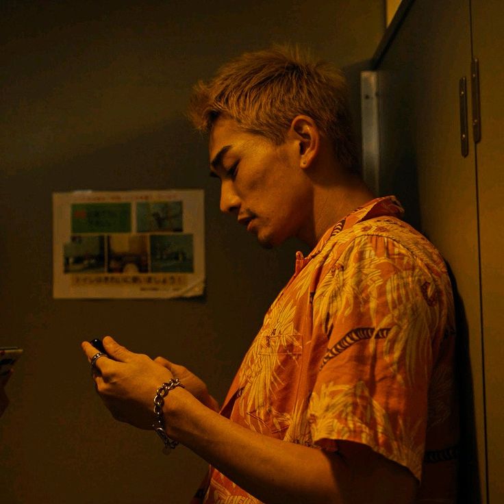 a young man looking at his cell phone in the dark, while leaning against a wall