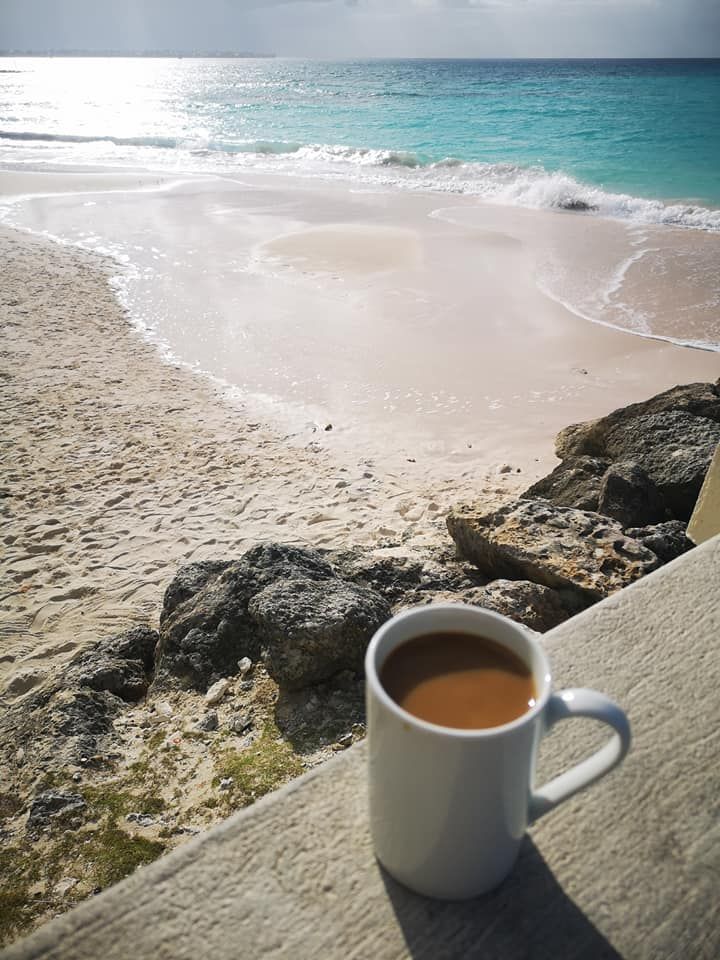 a cup of coffee sitting on top of a wooden table next to the ocean and beach