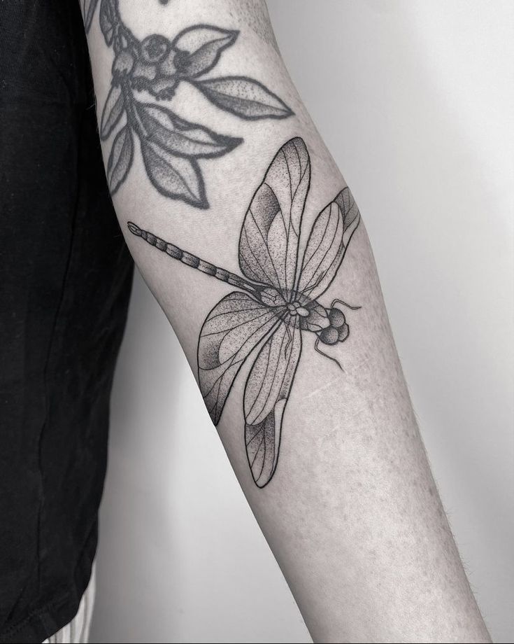 a black and white photo of a dragonfly tattoo on the right arm with an arrow