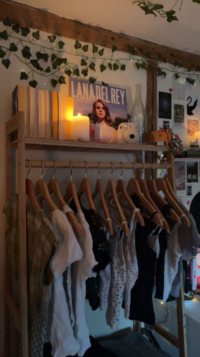 a rack with clothes hanging on it in a room next to a candle and bookshelf