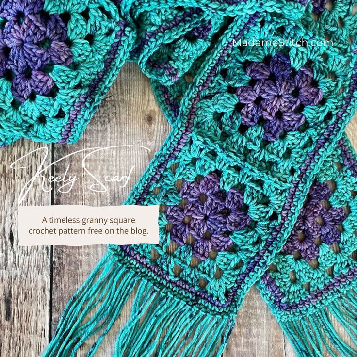 a crocheted scarf with purple and blue flowers on it, sitting on a wooden surface