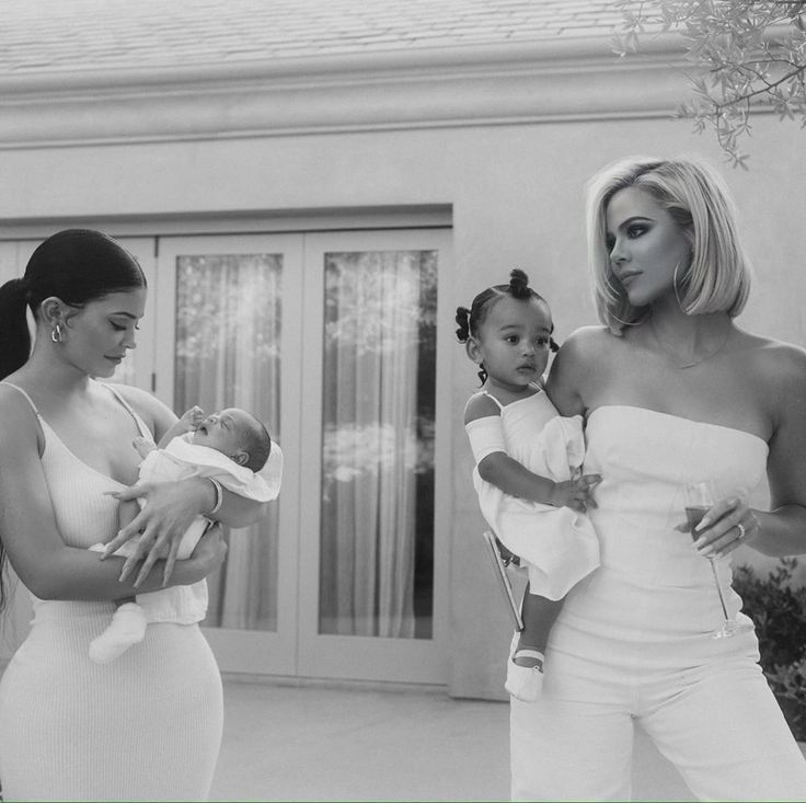 two women and a baby are standing outside in front of a house with their mother