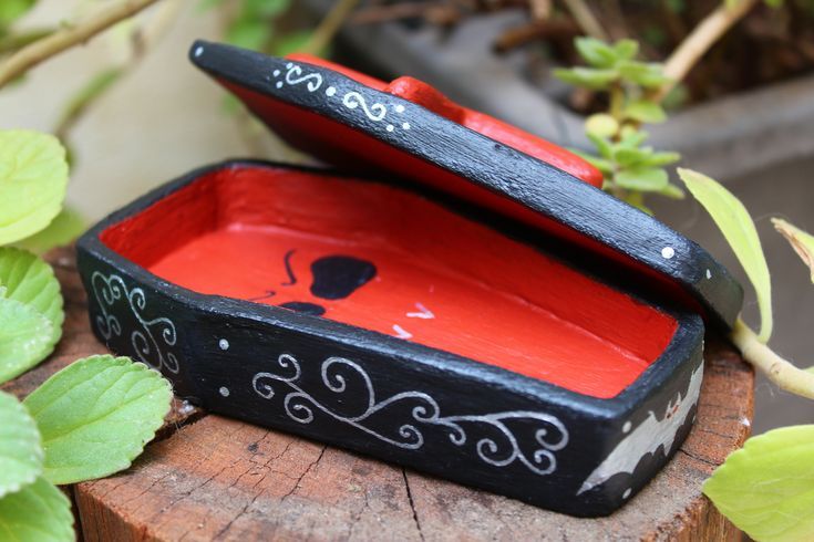 a red and black box sitting on top of a wooden stump next to green leaves