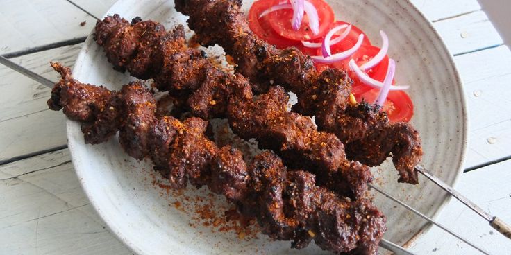 the skewers are being served with tomato slices and onions on the plate, ready to be eaten