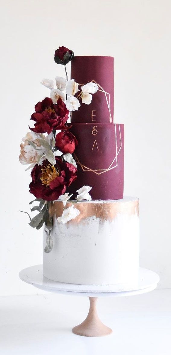 a three tiered cake with red and white flowers on the top is decorated with gold foil