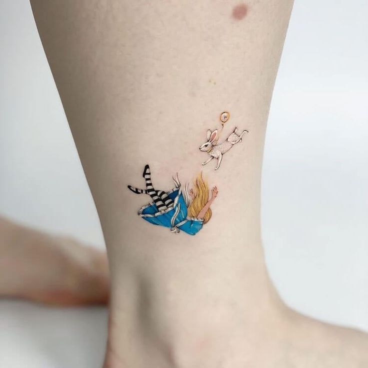 a small tattoo on the ankle of a woman's leg with alice and wonderland characters