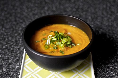 a black bowl filled with soup on top of a green and white place mat next to a spoon