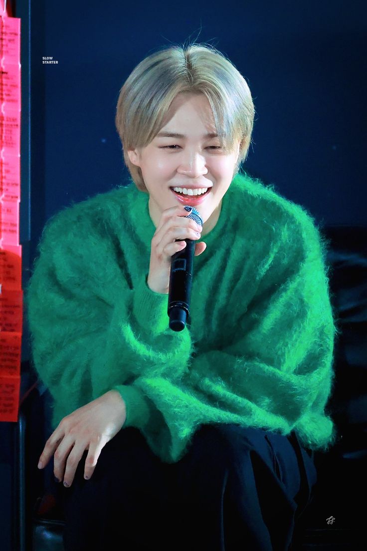 the young man is smiling while holding a microphone in his hand and wearing a green sweater