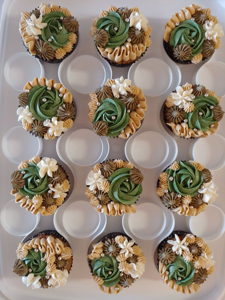 twelve cupcakes with green and white frosting in a plastic tray on a table