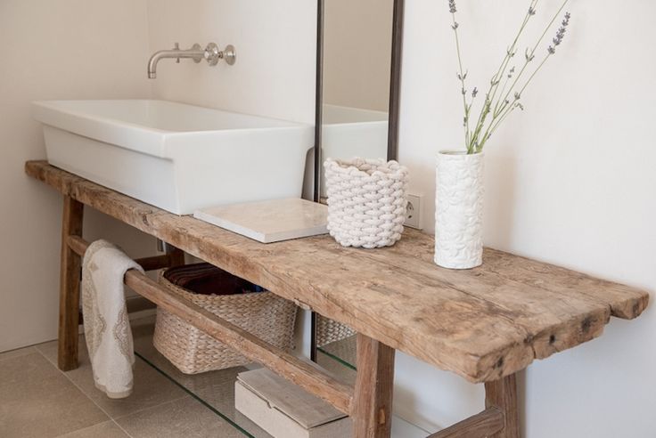 a wooden table topped with a white sink next to a mirror and vase filled with flowers