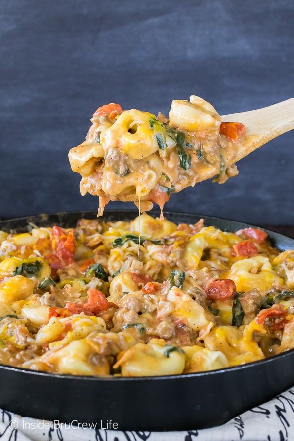 a wooden spoon scooping some food out of a skillet filled with macaroni and cheese