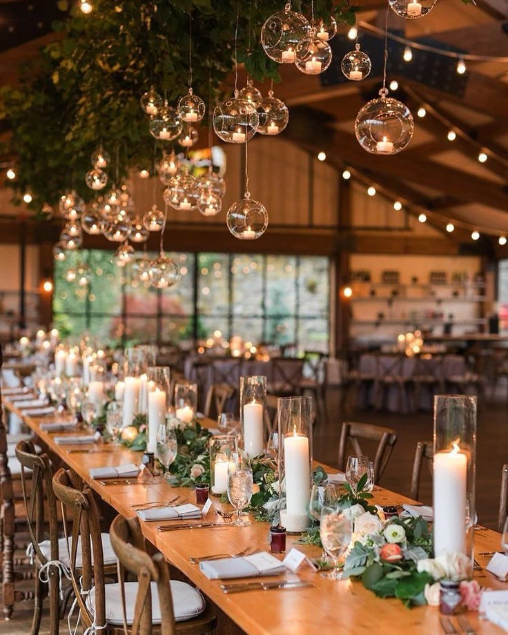 a long table with candles and greenery on it is surrounded by hanging glass globes