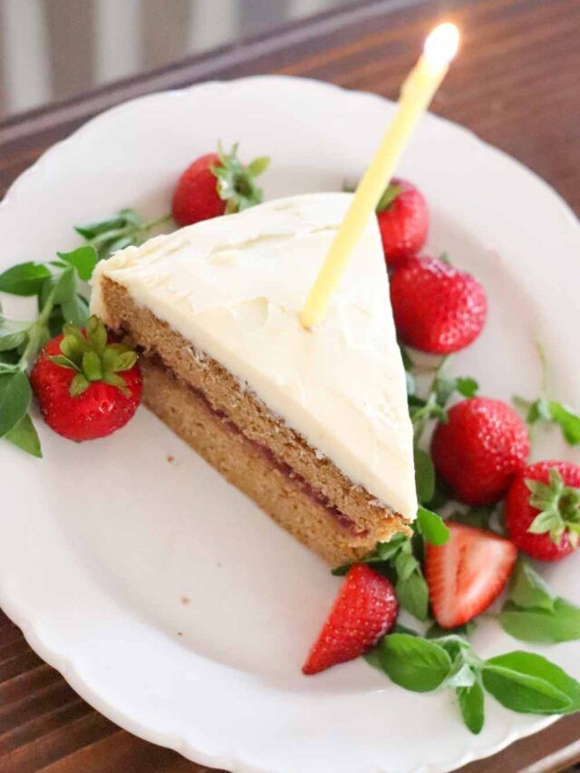 a slice of cake with white frosting and strawberries on a plate next to a lit candle