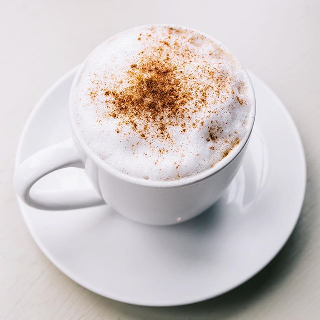 a cup of hot chocolate with cinnamon sprinkles and a spoon on a white plate