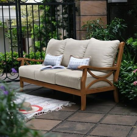 a wooden couch sitting on top of a patio next to some bushes and flowers in front of a gate