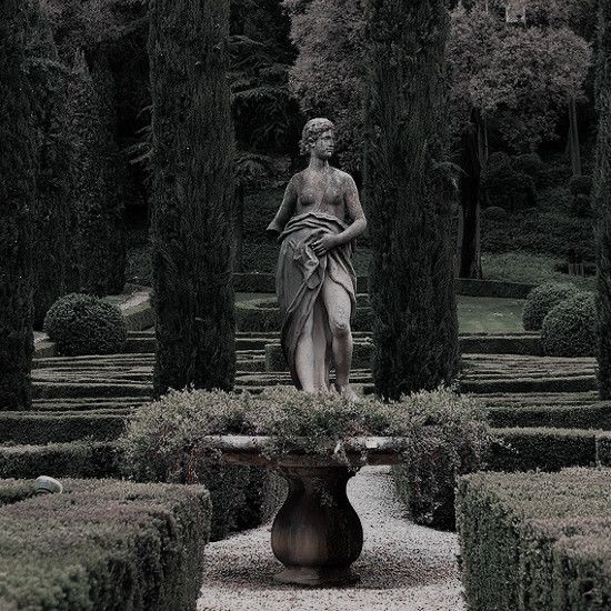 a statue in the middle of a garden surrounded by trees