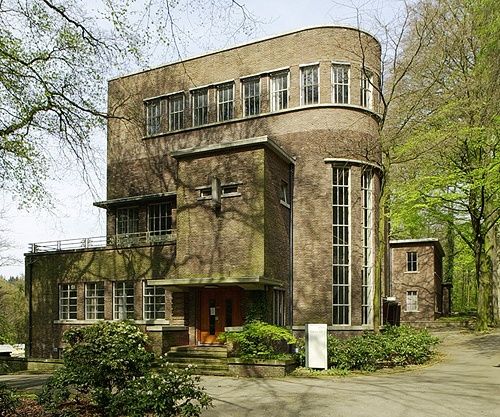 an old brick building with lots of windows on the front and side of it, surrounded by trees