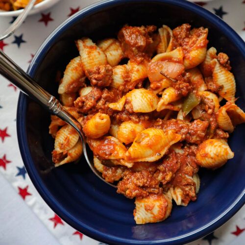 a blue bowl filled with pasta and meat on top of a white table cloth next to bowls of macaroni and cheese