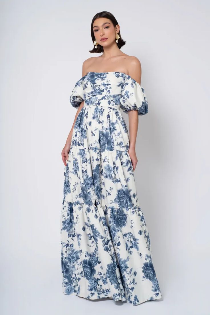 a woman wearing a blue and white floral print dress with off the shoulder, side view