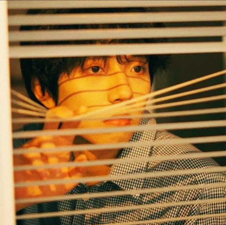 a man is looking through the blinds in front of him