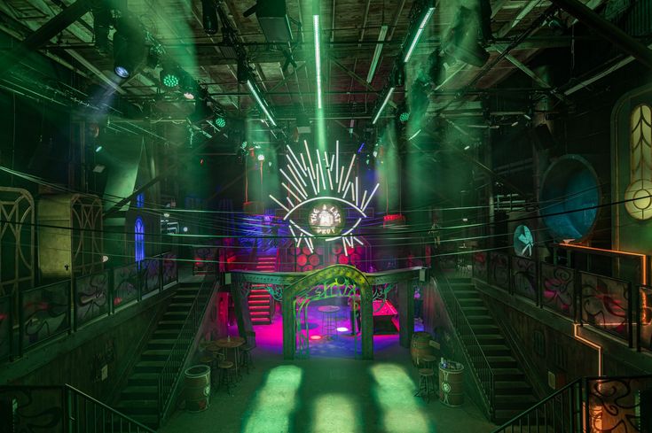 the inside of a building with green and pink lights on it's walls, stairs and railings