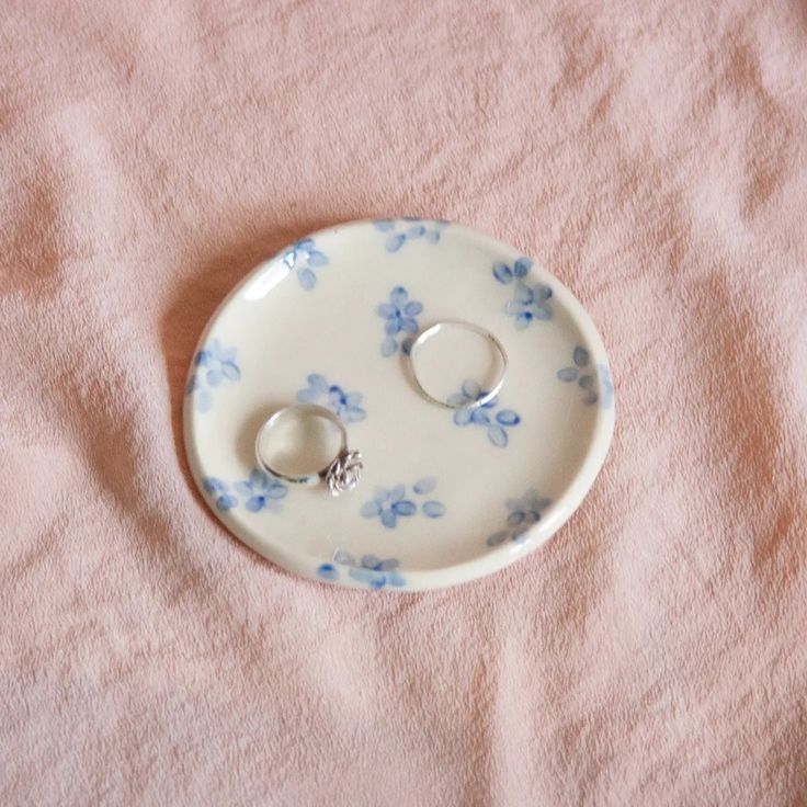 two wedding rings are placed on a blue and white flowered porcelain plate with pink linen