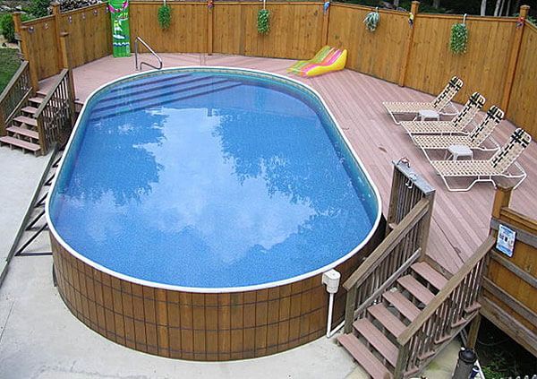 an above ground swimming pool surrounded by wooden decking and fenced in area with lounge chairs