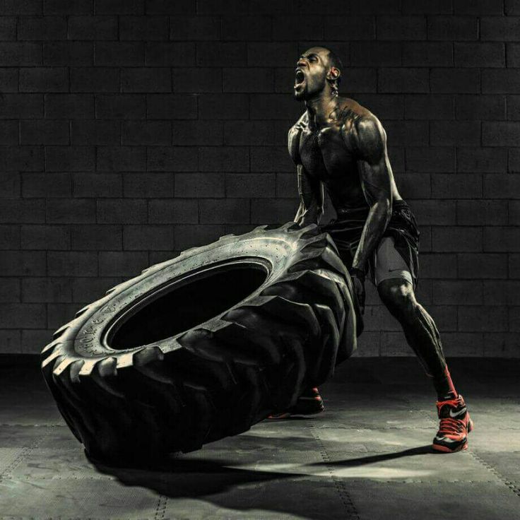 a man standing next to a giant tire in a dark room with bricks on the wall