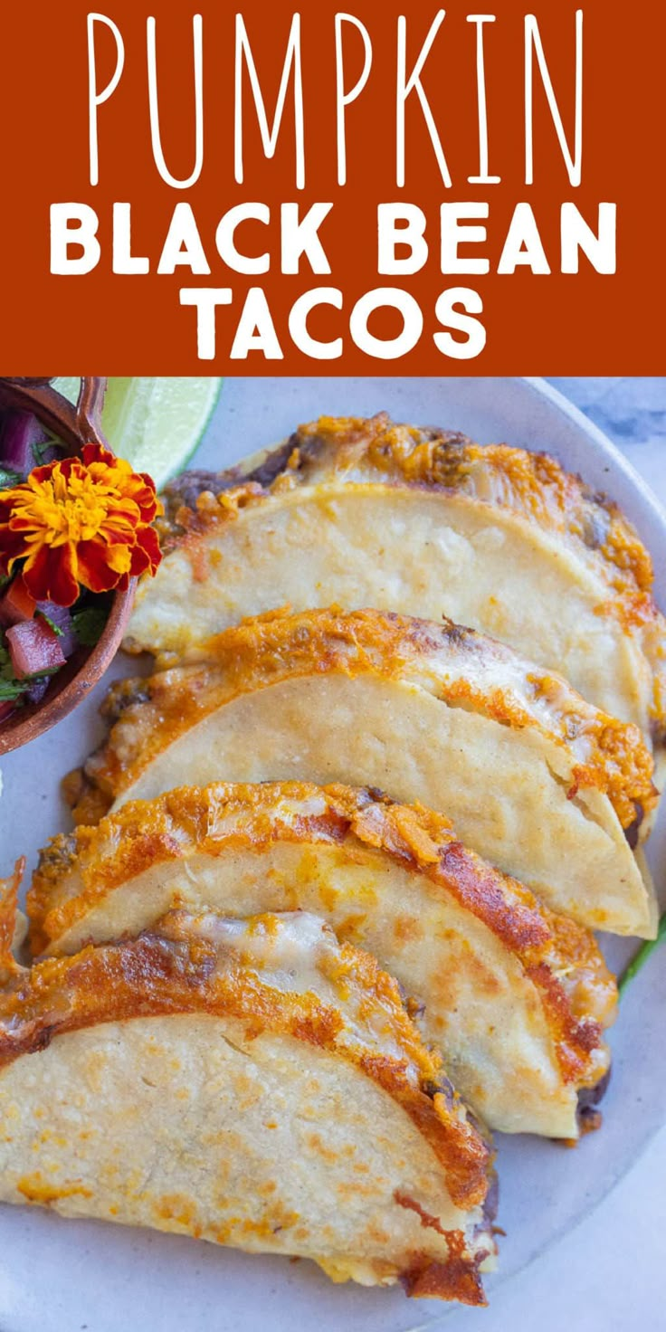 pumpkin black bean tacos on a white plate with a bowl of flowers in the background