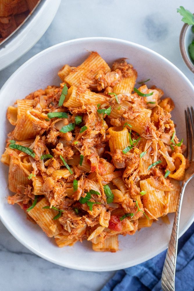 a white bowl filled with pasta covered in meat and sauce on top of a marble table