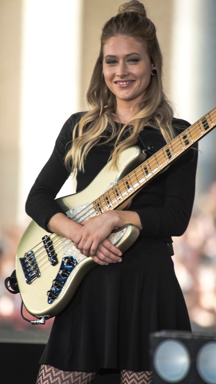 a woman is holding a guitar and smiling at the camera while standing in front of an audience