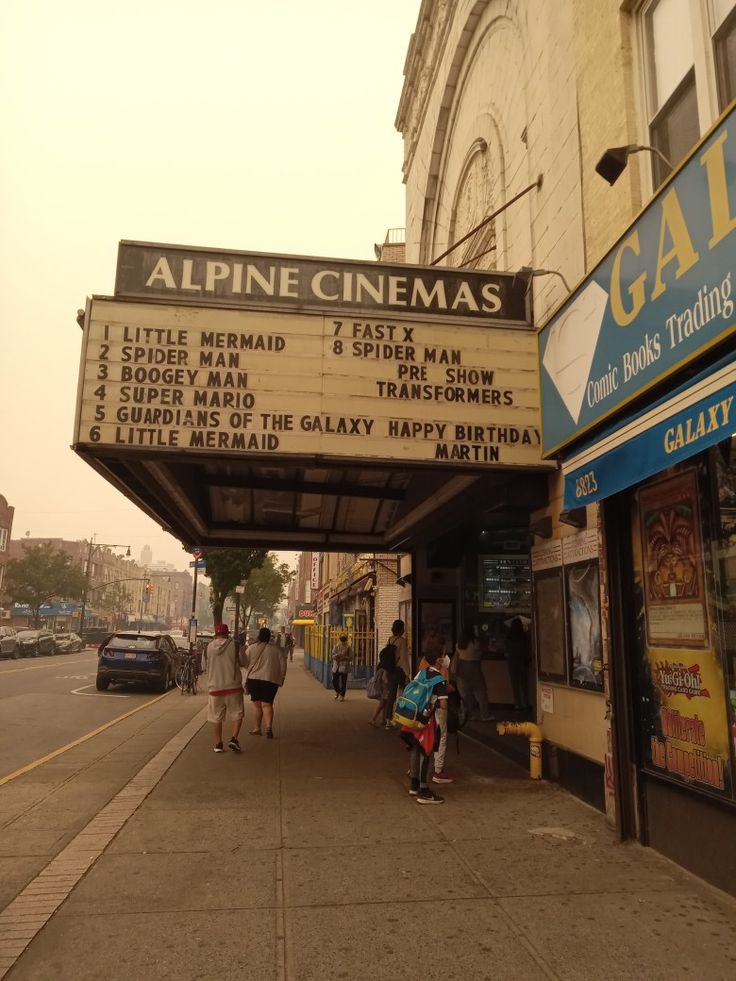 people are walking down the sidewalk in front of a movie theater