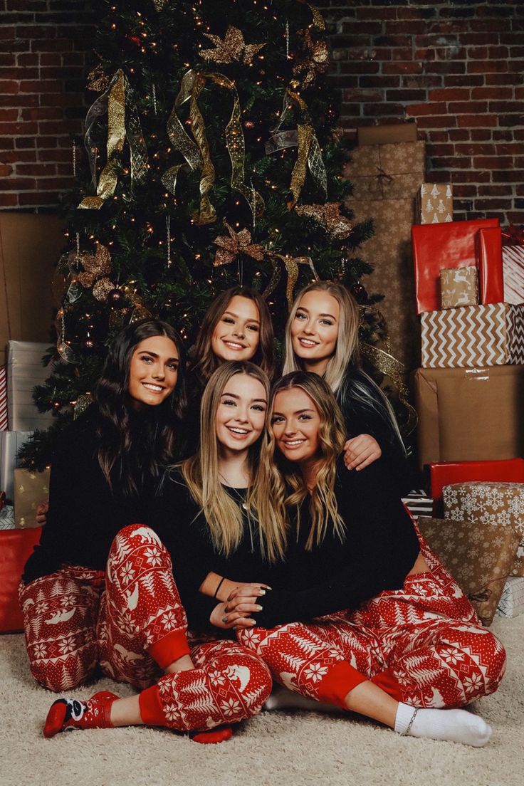 four women sitting in front of a christmas tree wearing matching pajamas and smiling at the camera