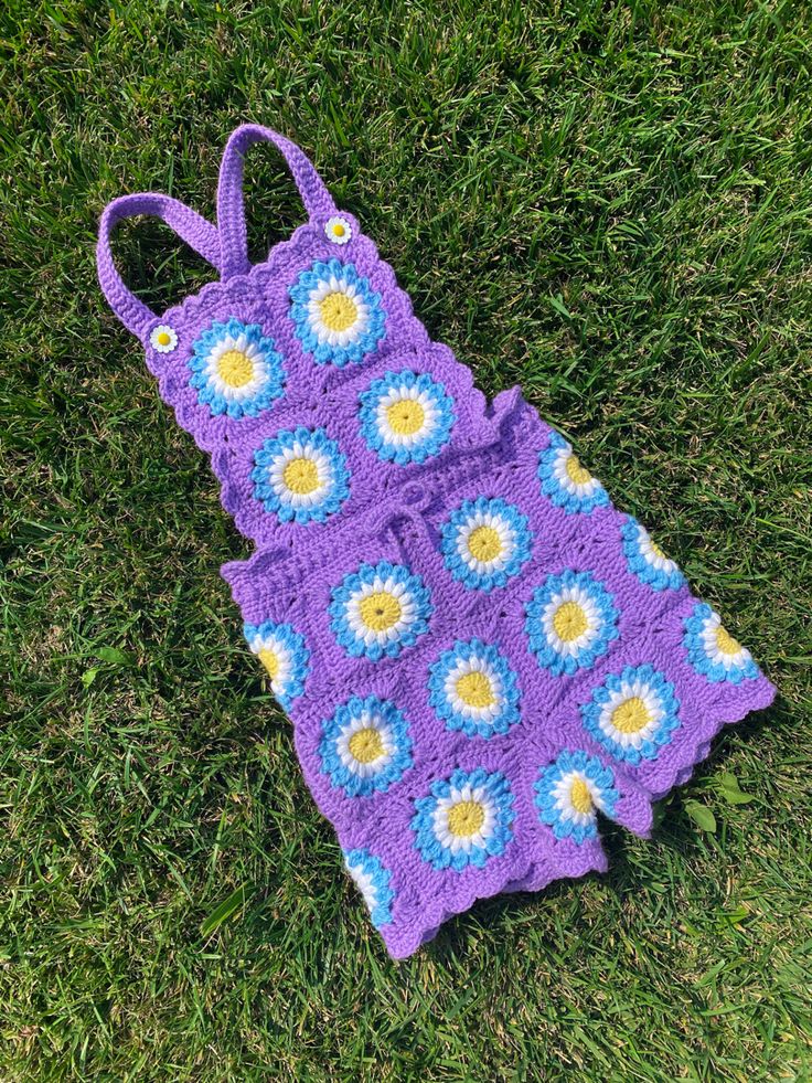 a purple crocheted bag laying on the grass with flowers in it's center