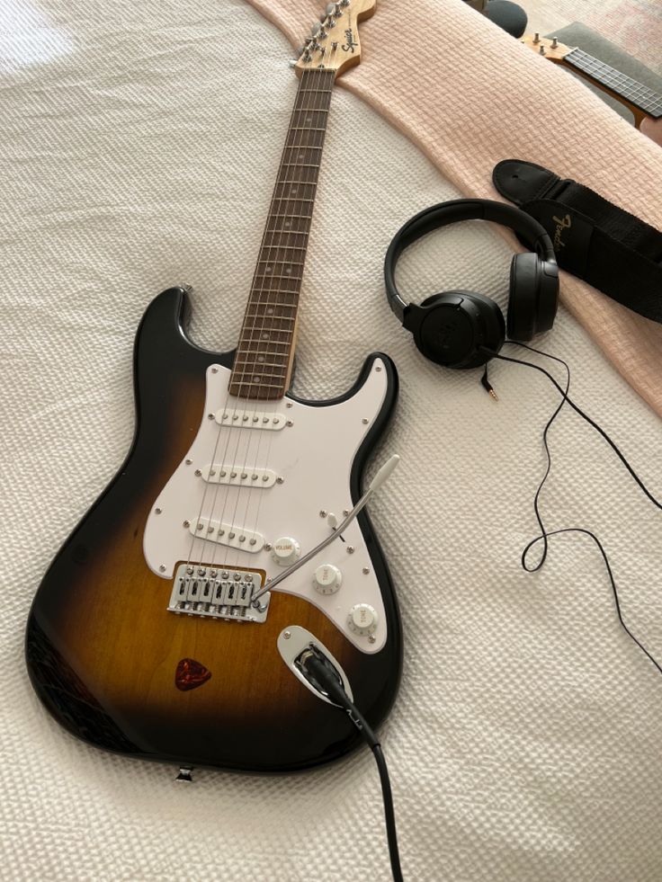 an electric guitar and headphones on a bed