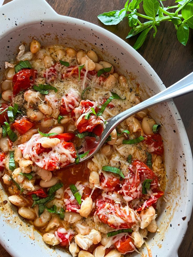 a white bowl filled with beans, tomatoes and basil on top of a wooden table