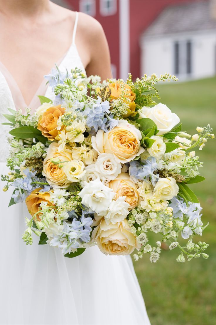 a bride holding a bouquet of flowers in her hand on the grass near a barn